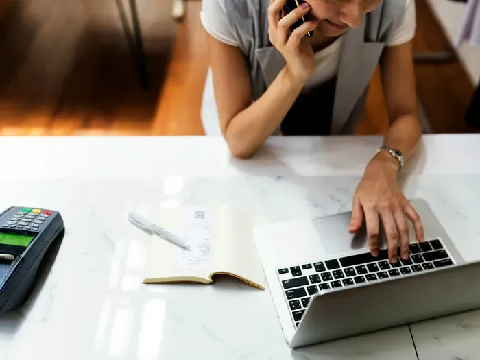 Woman multitasking by phone and laptop with notebook, representing small business owners managing services